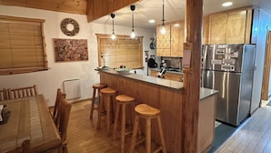 A wooden interior with a dining area, bar stools, and a kitchen with a refrigerator and stove. - Pine Lodge - 9 beds;  Extra fees  for 7+ Hot Tub Sauna AC EV Charger Pets (Packwood)