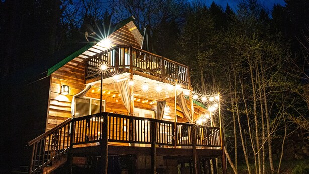 A two-story wooden cabin with a balcony, surrounded by trees, under a night sky with a visible moon. - Pine Lodge - 9 beds;  Extra fees  for 7+ Hot Tub Sauna AC EV Charger Pets (Packwood)