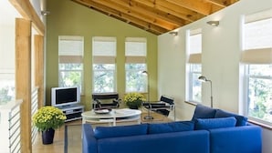 A modern living room with a wooden ceiling, a blue sofa, a TV, and a table with a lamp.