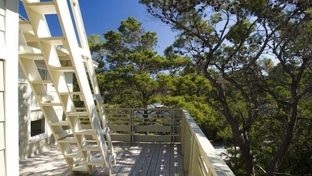 A wooden deck with a white railing, overlooking a forested area.