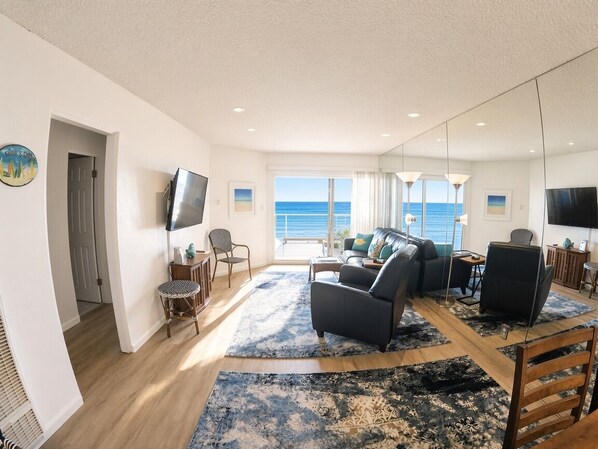 A modern living room with a large window, a flat-screen TV, and a seating area with a sofa and chairs.