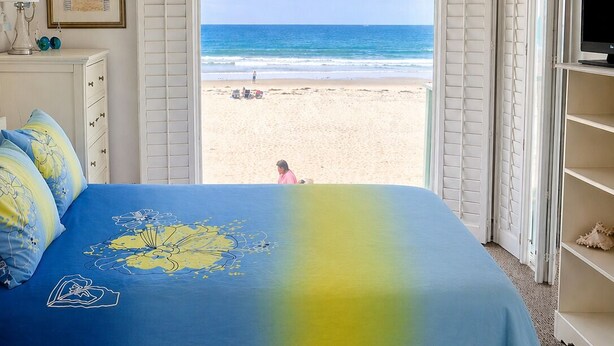 A bedroom with a bed, a dresser, a TV, and a view of the beach.