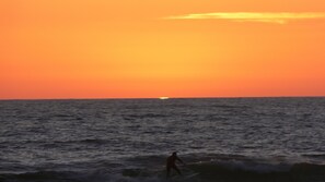 Een ondergaande zon boven de oceaan, silhouet van een persoon die aan het surfen is.