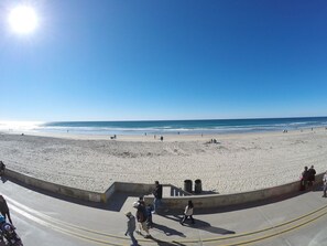 A beach with a concrete walkway, people walking, and the ocean in the background.