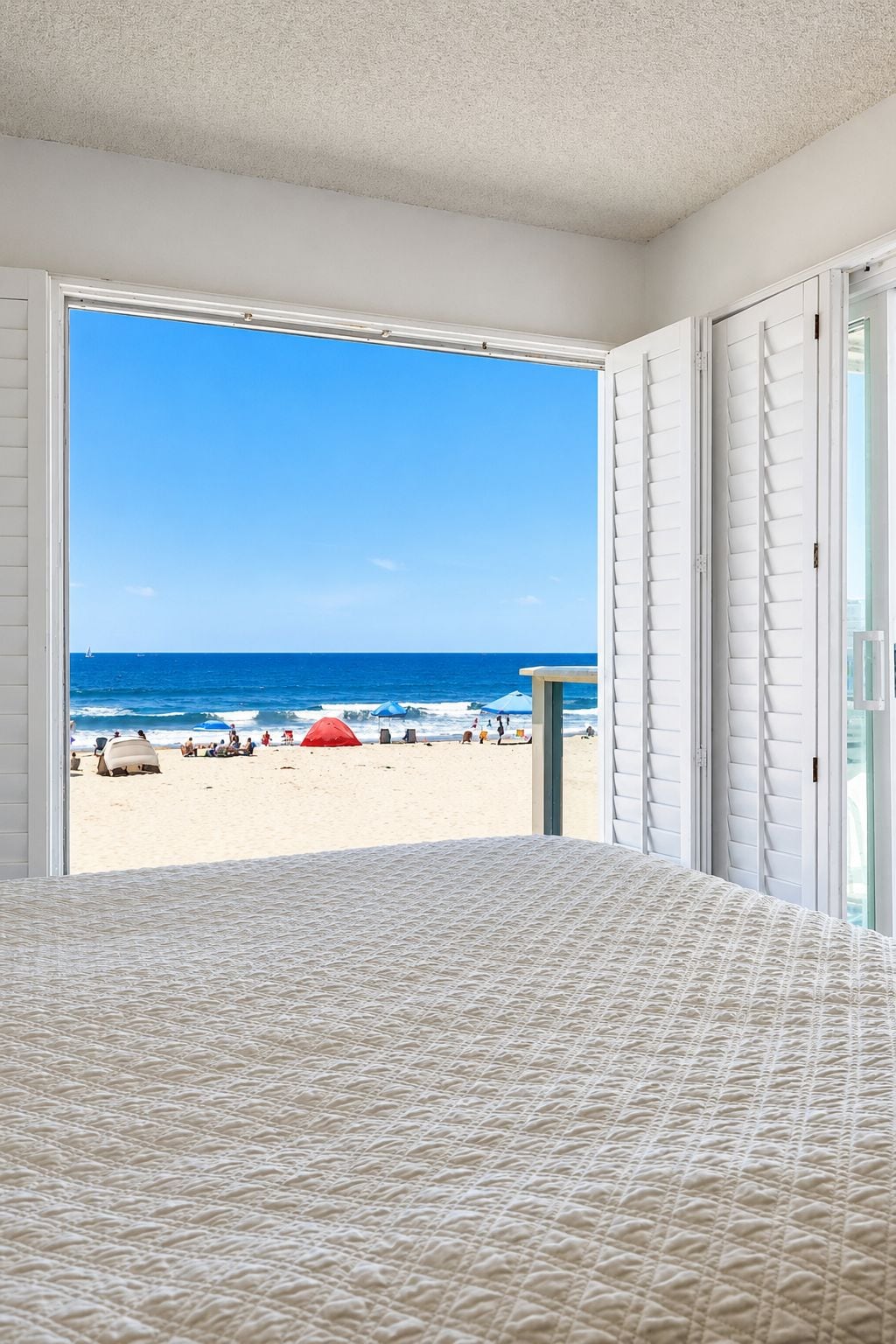A room with a large bed and a view of a beach with umbrellas.