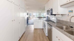 A modern kitchen with white cabinetry, a granite countertop, stainless steel appliances, and a view to the dining area.
