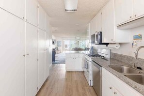 Una cocina moderna con muebles blancos, encimera de granito, electrodomésticos de acero inoxidable y vistas al comedor.