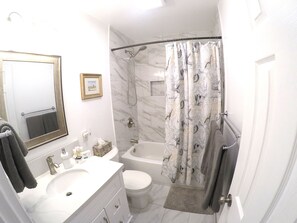 Een badkamer met een wit wastafel, toilet, bad en douchegordijn met een vogelmotief.