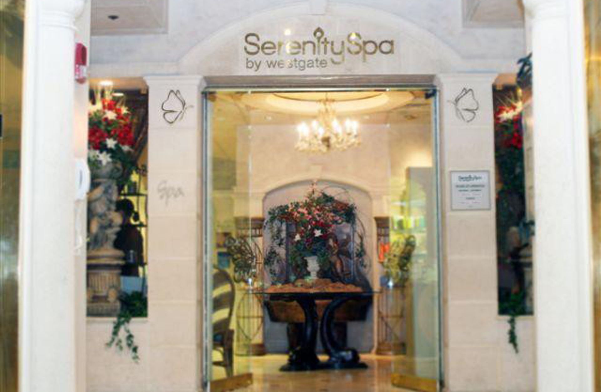 L’entrée du spa Serenity, avec une porte en verre, un lustre et des décorations florales.
