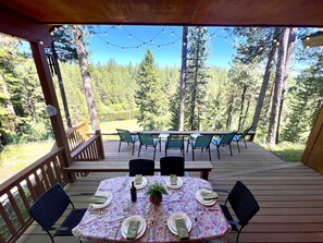 A wooden deck with a table set for four, surrounded by chairs, overlooking a forested area. - On the Payette River - beauty, comfort, gourmet kitchen  (McCall)
