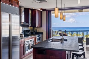 Een moderne keuken met een groot eiland, roestvrijstalen apparatuur en uitzicht op de oceaan.
