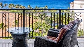 Un balcon doté d'une table en verre et de meubles en osier, offrant une vue sur une plage et l'océan.