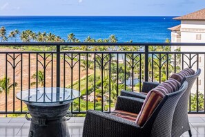 Een balkon met een glazen tafel en rieten meubilair met uitzicht op een strand en de oceaan.