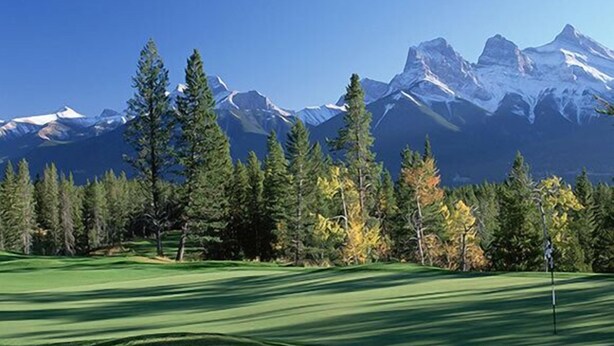 A golf course with a flagstick, surrounded by trees and mountains in the background.