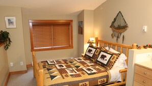 A bedroom with a wooden bed, a window with blinds, a wall-mounted fish net, and a bedside lamp.