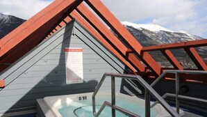 A hot tub with a view of snow-capped mountains, a wooden deck, and a safety sign.