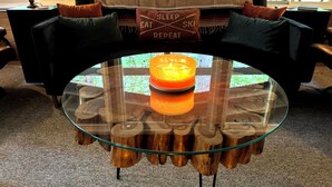 A cozy living room with a glass coffee table featuring wooden logs, a sofa with colorful cushions, and a 'SLEEP EAT SKI REPEAT' pillow. - Private 5 Acres in Packwood, close to Cowlitz River, Mt. Rainer & White Pass. (Packwood)