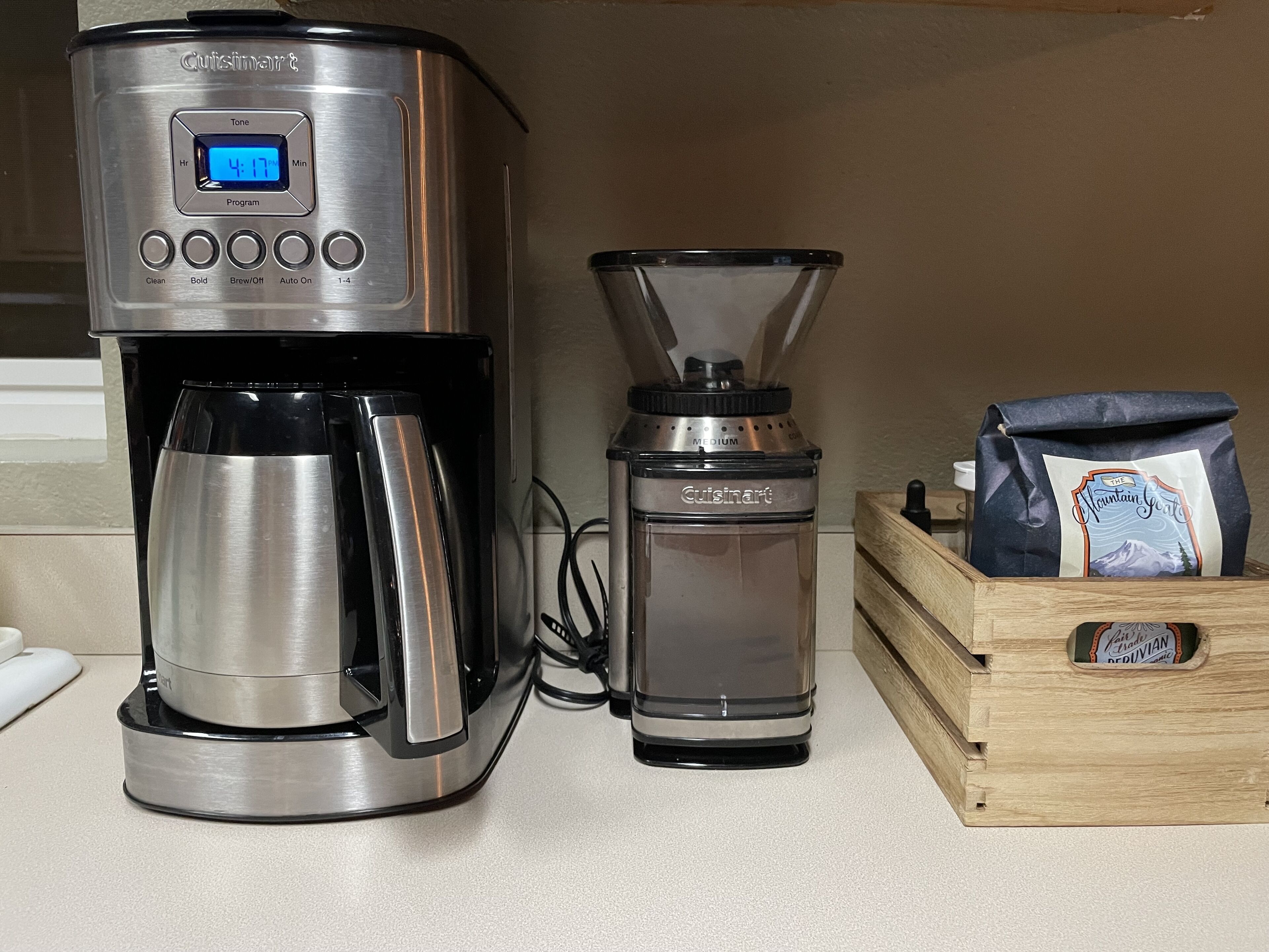 Een koffiezetapparaat, een koffiemolen en een zak koffiebonen op een aanrecht.