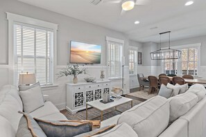 Uma sala de estar moderna com um sofá branco, uma mesa de centro e um espaço de jantar com mesa e cadeiras.