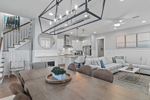 A modern kitchen with white cabinets, a stainless steel range hood, and a dining area with a wooden table and wicker chairs. - 6-Seater Golf Cart & 6 Bikes! Newly Furnished! 2 Resort Pools! Sunset at Seagrove on 30A (Santa Rosa Beach)