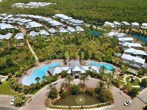 An aerial view of a resort with multiple buildings, a central pool, and surrounding greenery. - 6-Seater Golf Cart & 6 Bikes! Newly Furnished! 2 Resort Pools! Sunset at Seagrove on 30A (Santa Rosa Beach)