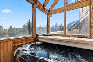 Una vasca idromassaggio con pareti in legno e ampie finestre che si affacciano su una foresta e montagne.