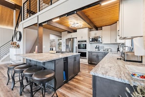 Una cucina moderna con un'ampia isola, sgabelli da bar, elettrodomestici in acciaio inossidabile e un soffitto in legno.
