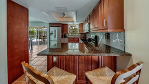 A kitchen with wooden cabinets, a granite countertop, and a dining area with wicker chairs. - Updated and Spacious 3 Bed 2 BA Home, Heated Pool, 4 Bikes, 5 Min Walk to Beach  (Marco Island)