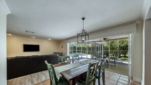 A dining area with a wooden table and chairs, a black sofa, and a TV mounted on the wall. - Updated and Spacious 3 Bed 2 BA Home, Heated Pool, 4 Bikes, 5 Min Walk to Beach  (Marco Island)
