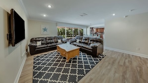 A spacious living room with a large sectional sofa, a coffee table, and a flat-screen TV mounted on the wall. - Updated and Spacious 3 Bed 2 BA Home, Heated Pool, 4 Bikes, 5 Min Walk to Beach  (Marco Island)