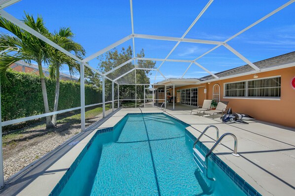 A swimming pool with a covered area, palm trees, and a house in the background. - Updated and Spacious 3 Bed 2 BA Home, Heated Pool, 4 Bikes, 5 Min Walk to Beach (Marco Island)