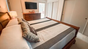A bedroom with a large bed, a dresser, a TV mounted on the wall, and a door leading to another room. -  Foodies Kitchen, Peaceful, Green, Comfiest Beds, Close to everything   (Olympia)