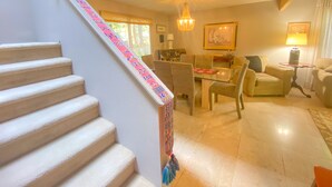 A staircase with a colorful handrail, a dining area with chairs and a table, a chandelier, and a lamp. -  Foodies Kitchen, Peaceful, Green, Comfiest Beds, Close to everything   (Olympia)