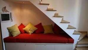 Ein rotes Sofa mit Stauraumschubladen darunter, vor einer weißen Wand mit einer Holztreppe.