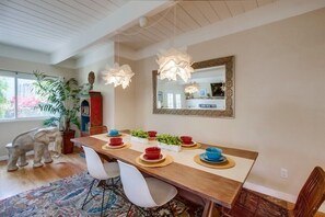 Comedor con mesa de madera, sillas blancas y un espejo encima.