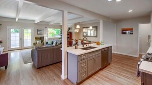 A modern kitchen with a central island, a dining area with a sofa, and a large window providing natural light. - Pacific Beach Escape | Walk to Ocean | Private Yard | A/C | Dogs OK (San Diego)