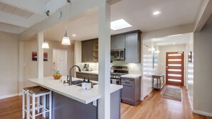 A modern kitchen with a central island, grey cabinets, and pendant lighting. - Pacific Beach Escape | Walk to Ocean | Private Yard | A/C | Dogs OK (San Diego)