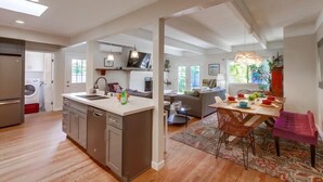 A modern kitchen with a central island, a dining area with a table and chairs, and a living room with a sofa and a coffee table. - Pacific Beach Escape | Walk to Ocean | Private Yard | A/C | Dogs OK (San Diego)