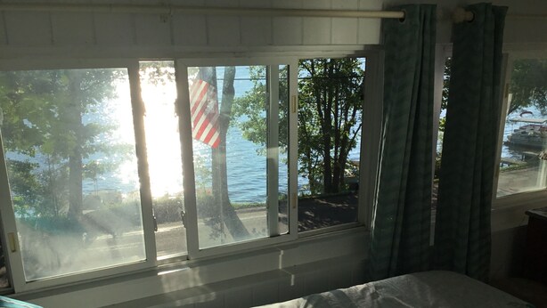 Een slaapkamer met uitzicht op een meer en bomen, een bed met een bloemenprint deken en een raam met gordijnen.