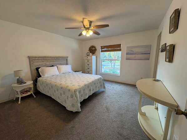 A bedroom with a bed, a nightstand, a dresser, a window with a view, and a ceiling fan.