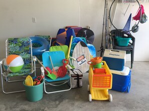 A storage area with beach and pool equipment, including chairs, a toy truck, and various containers.