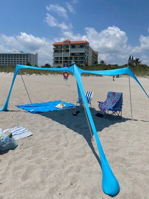 A beach with a blue canopy, two beach chairs, and a striped towel on the sand. - BIG BEAUTIFUL BEACH HOUSE- STEPS TO THE SAND- (Cocoa Beach)