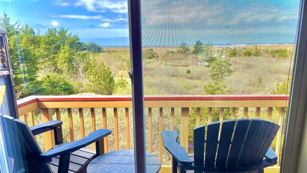 Un balcon donnant sur un espace verdoyant et des arbres, avec une table et deux chaises.
