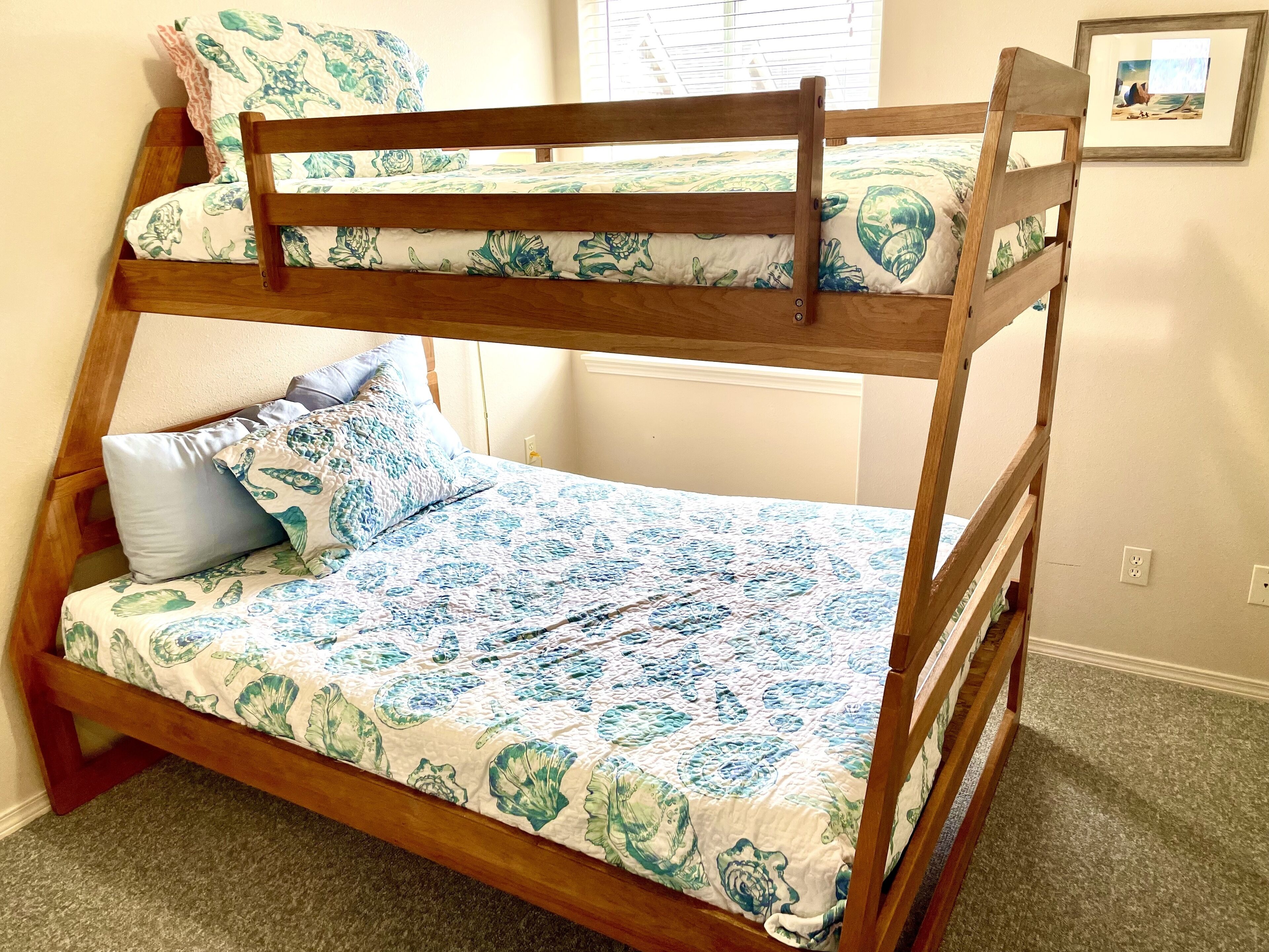 A bunk bed with floral bedding, a single bed with matching pillows, a window with blinds, and a framed picture on the wall.