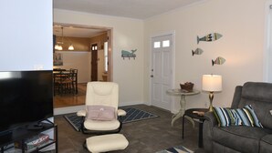 Una sala de estar con televisor, sofá, sillón, lámpara y peces decorativos en la pared.