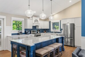 A modern kitchen with a large island, stainless steel appliances, and pendant lighting. - Luxury Macatawa Beach Home with Stunning Lake Michigan Views (Holland)