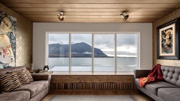 Ein Zimmer mit großem Fenster mit Blick auf einen See und Berge, zwei Sofas, Holzboden und ein gemustertes Teppich.