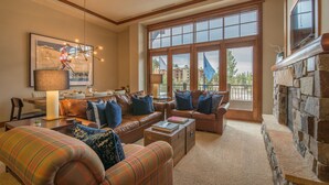 A spacious living room with leather sofas, a fireplace, large windows, and a dining area. - Luxury 3BD Village at Northstar Residence - Iron Horse North 101 (Truckee)