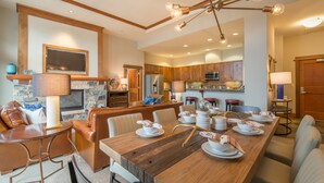 A spacious dining area with a long wooden table set for a meal, flanked by leather sofas and a stone fireplace. - Luxury 3BD Village at Northstar Residence - Iron Horse North 101 (Truckee)