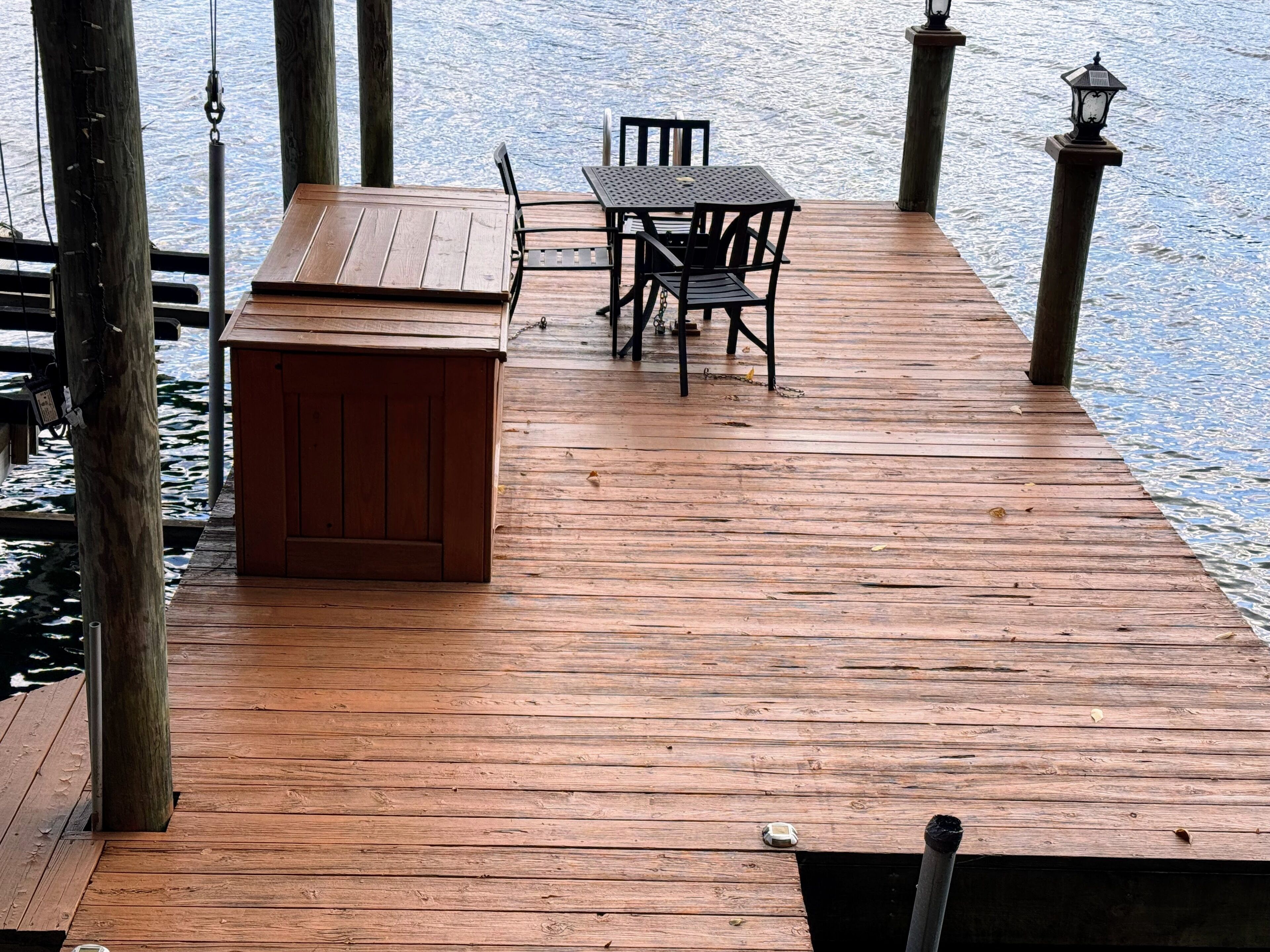 A wooden dock with a table and chairs, a wooden cabinet, and a lantern post.